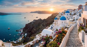 Panoramic golden hour view of whitewashed houses and blue-domed churches in Oia, Santorini, overlooking the Aegean Sea volcanic caldera.